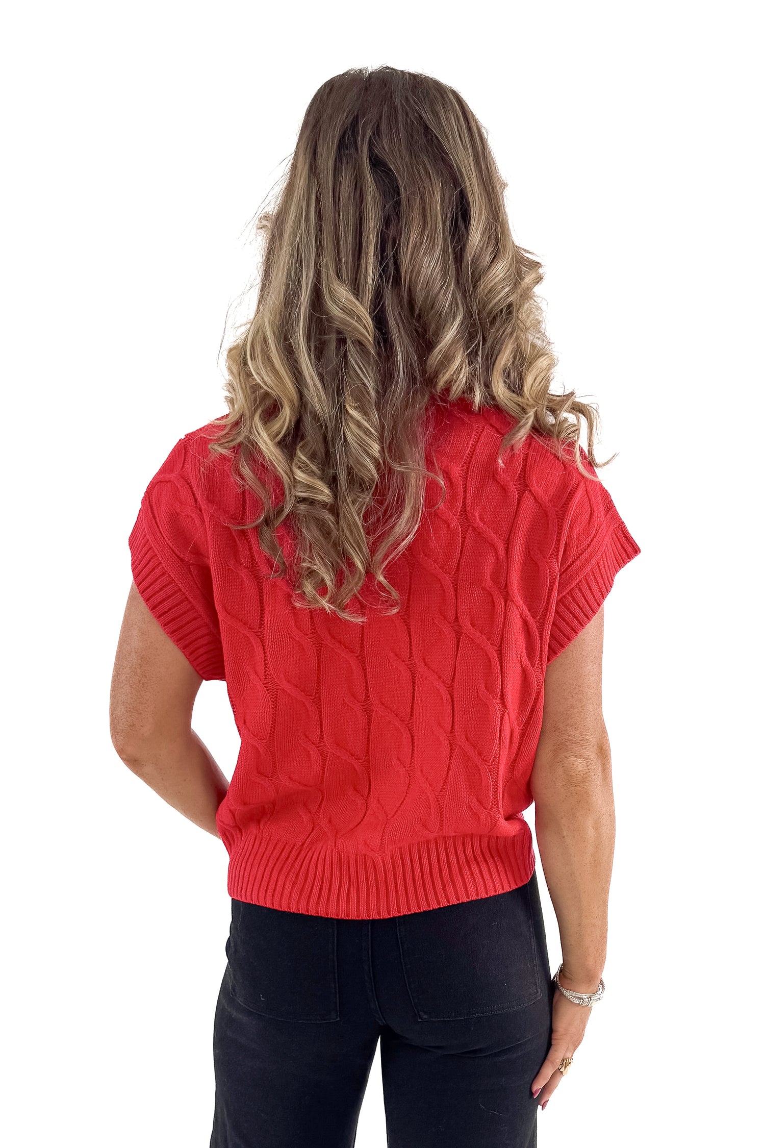 Back view of woman wearing red sleeveless sweater with jeans against white studio background.