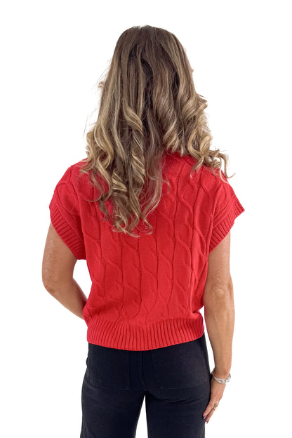 Back view of woman wearing red sleeveless sweater with jeans against white studio background.
