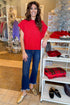 Front view of woman wearing red sleeveless sweater with jeans at a boutique.