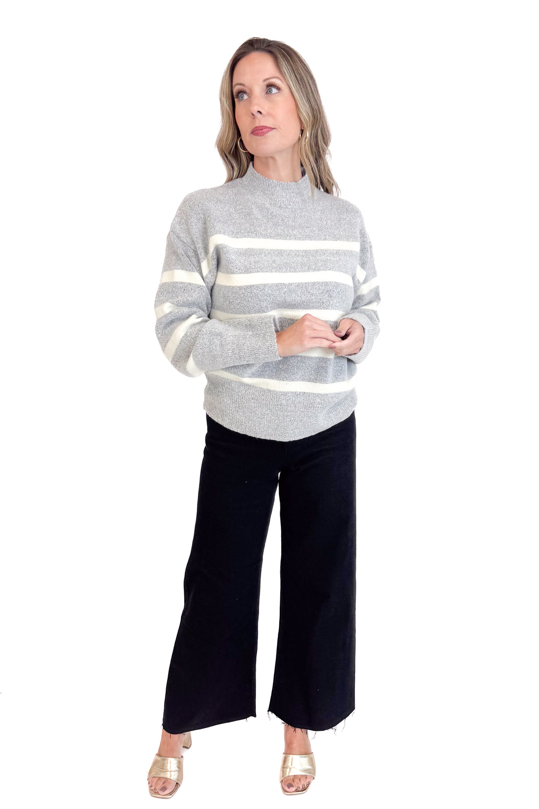 Woman wearing a gray sweater with white stripes and black pants on a white background
