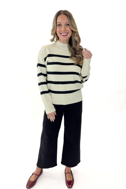 Front full view of woman wearing Black &amp; Cream Striped Mock Neck Sweater with jeans against white studio background.