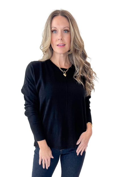 Front view of woman wearing Black Center Seam Round Neck Sweater with jeans against white studio background.