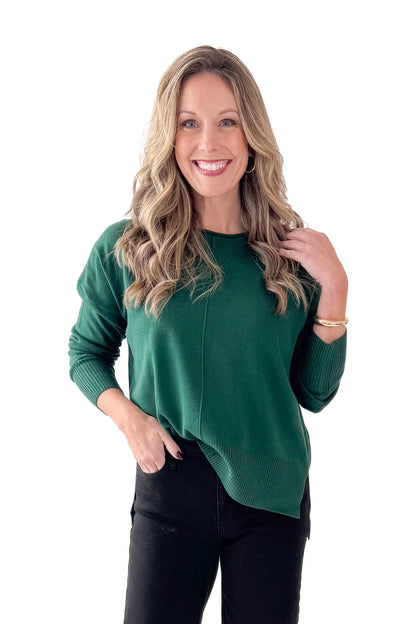 Front view of woman wearing Green Center Seam Round Neck Sweater with jeans against white studio background.