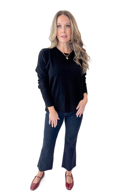 Front view of woman wearing Black Center Seam Round Neck Sweater with jeans against white studio background.
