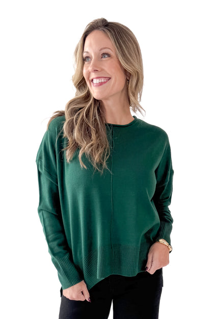 Front view of woman wearing Green Center Seam Round Neck Sweater with jeans against white studio background.