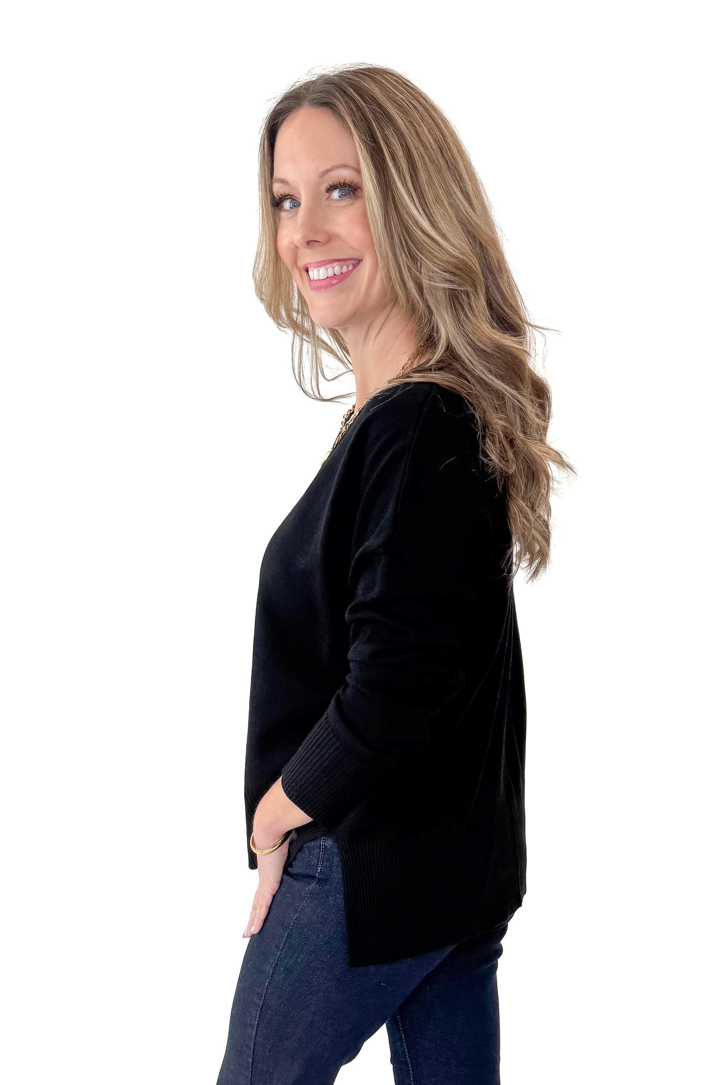 Side view of woman wearing Black Center Seam Round Neck Sweater with jeans against white studio background.