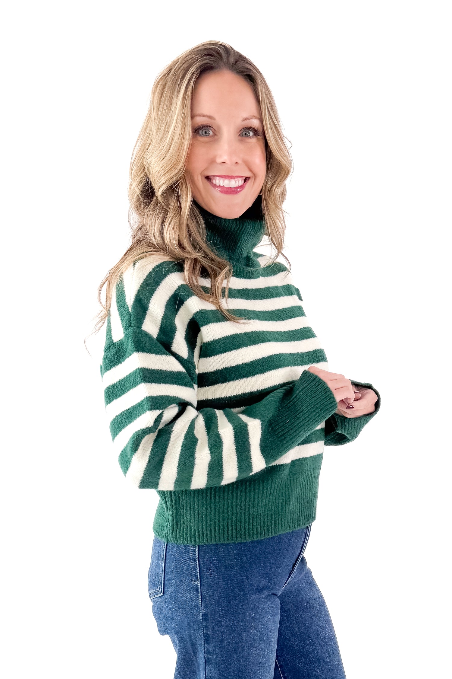 Side view of woman wearing Green &amp; Cream Striped Turtleneck Sweater with jeans against white studio background.