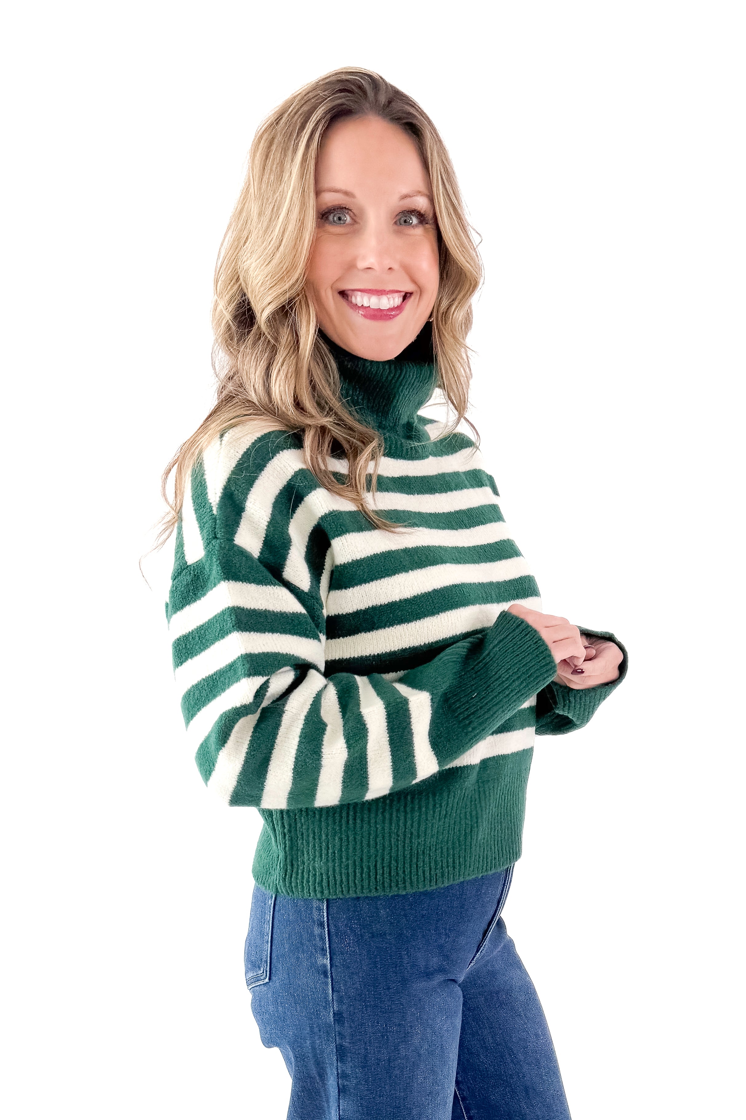 Side view of woman wearing Green &amp; Cream Striped Turtleneck Sweater with jeans against white studio background.