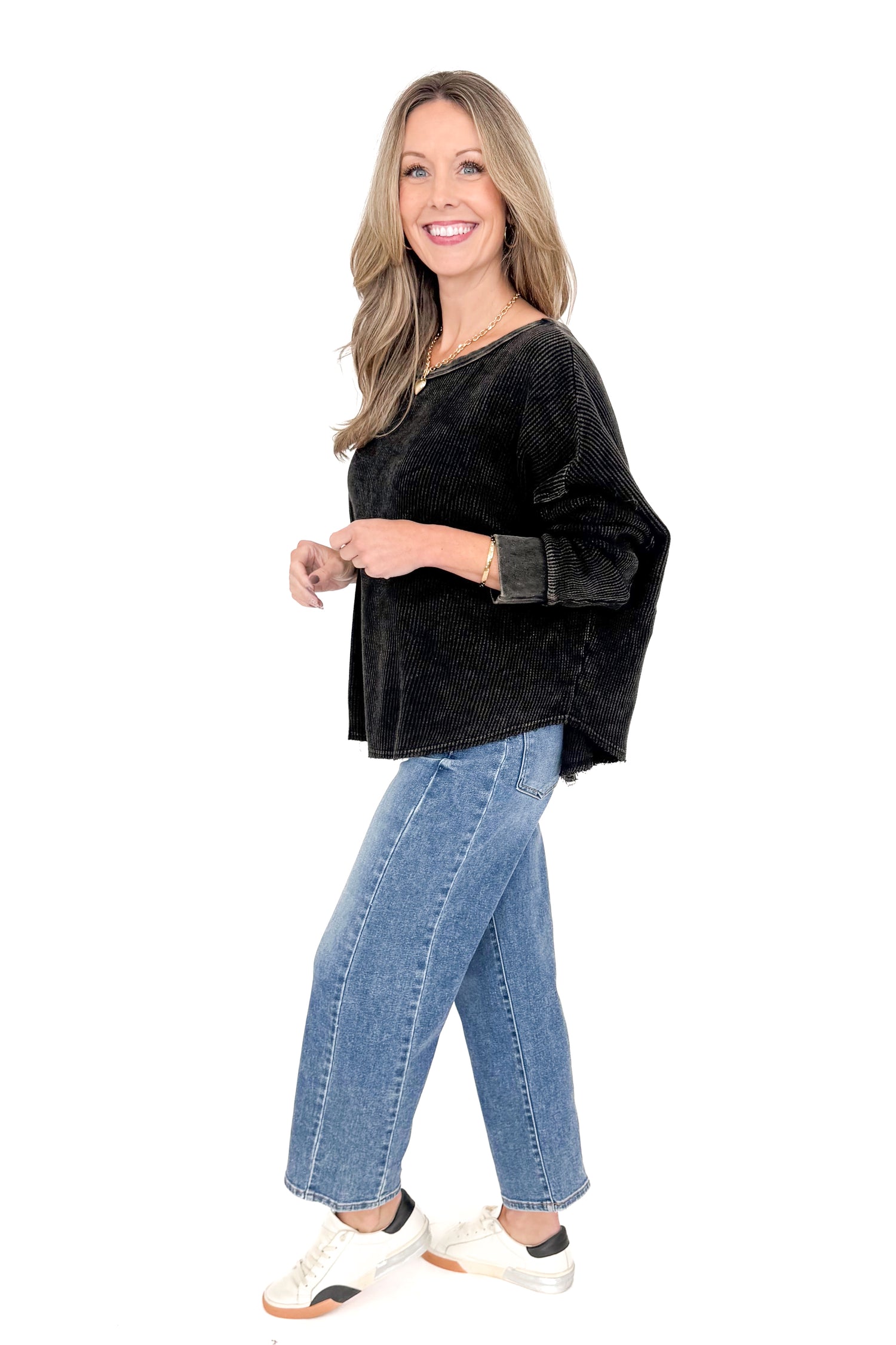 Side view of woman wearing washed black waffle top with jeans against white studio background.