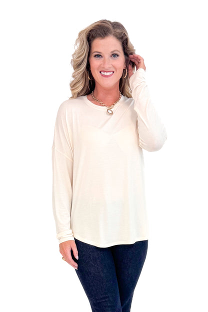 Front view of woman with cream long sleeve curve hem top and blue jeans.