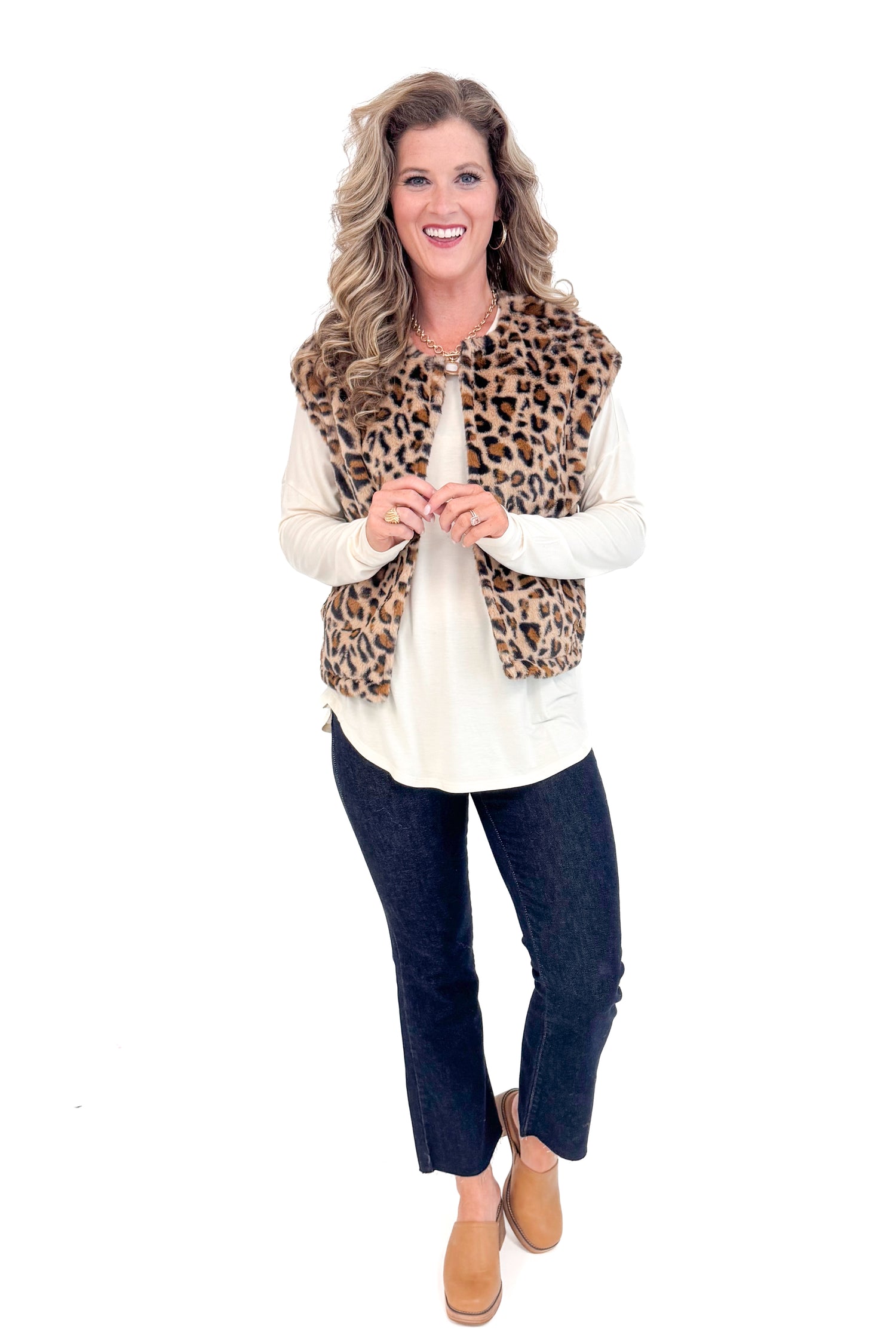 Front view of woman with cream long sleeve curve hem top and blue jeans and leopard jacket.