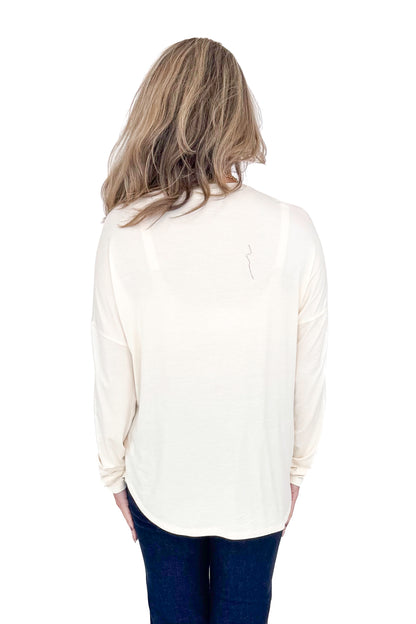 Back view of woman with cream long sleeve curve hem top and blue jeans against white studio background.