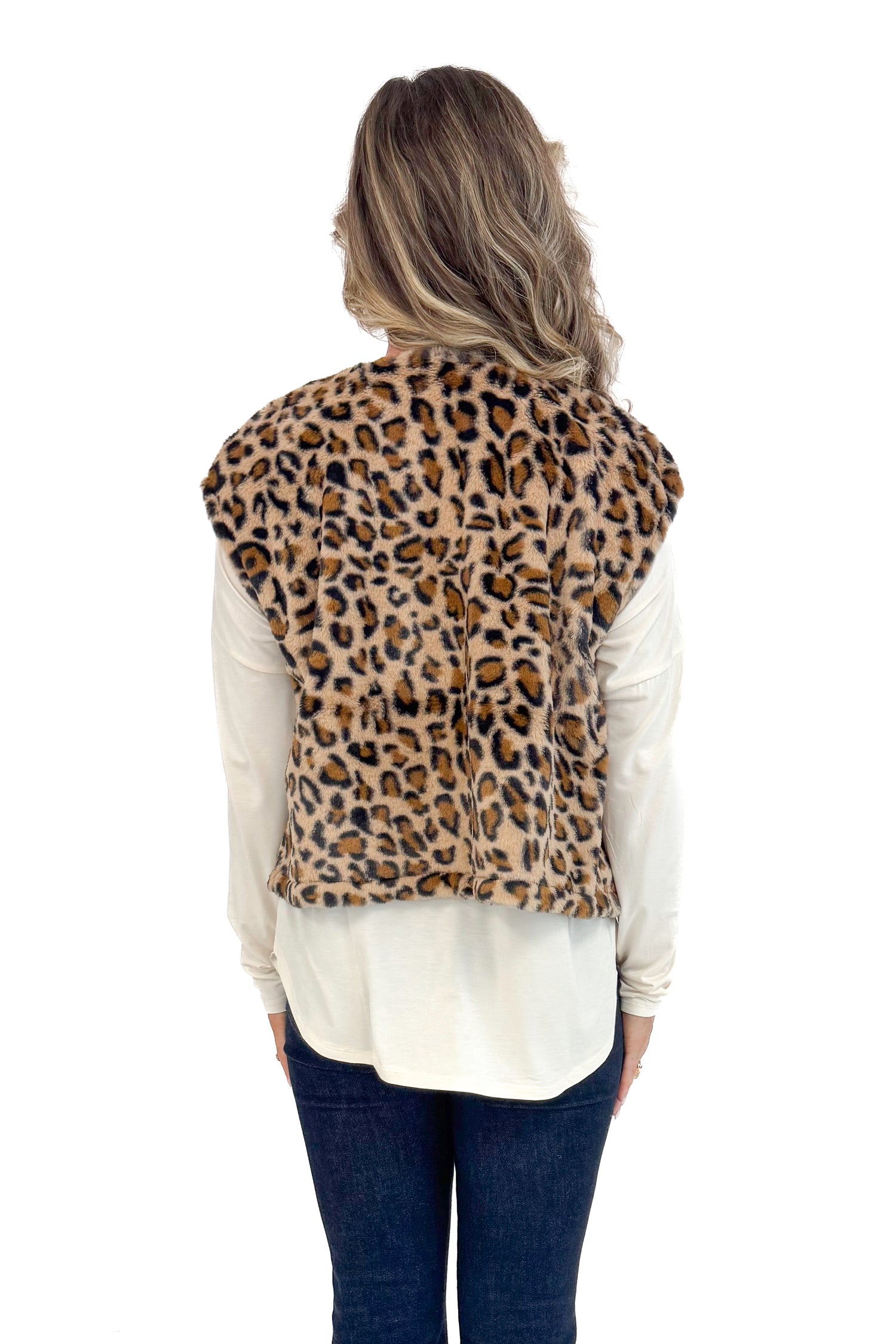 Back view of woman with cream long sleeve curve hem top and blue jeans and leopard jacket.
