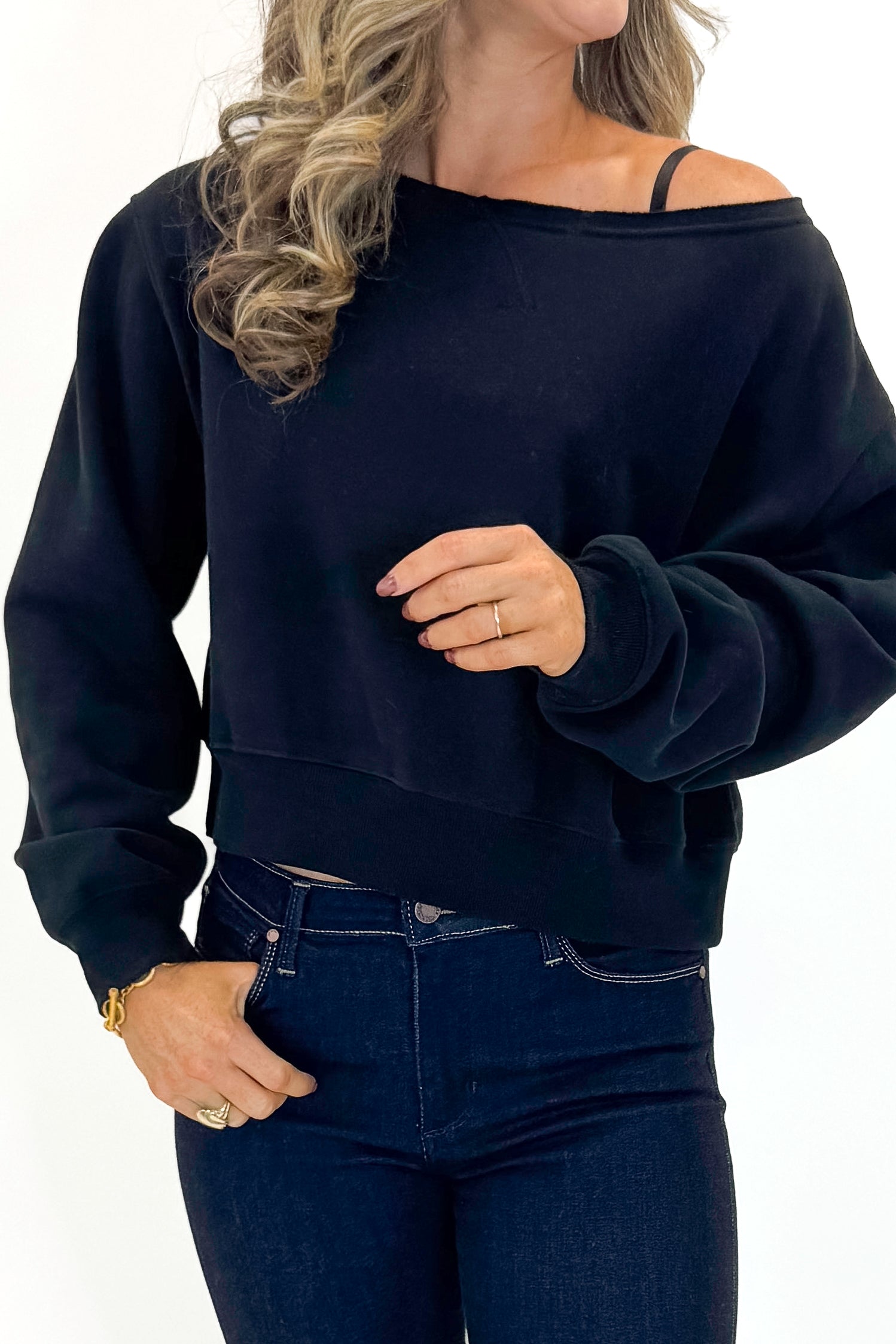 Front detail view of woman wearing Black Boatneck Banded Sweatshirt with jeans against white studio background.