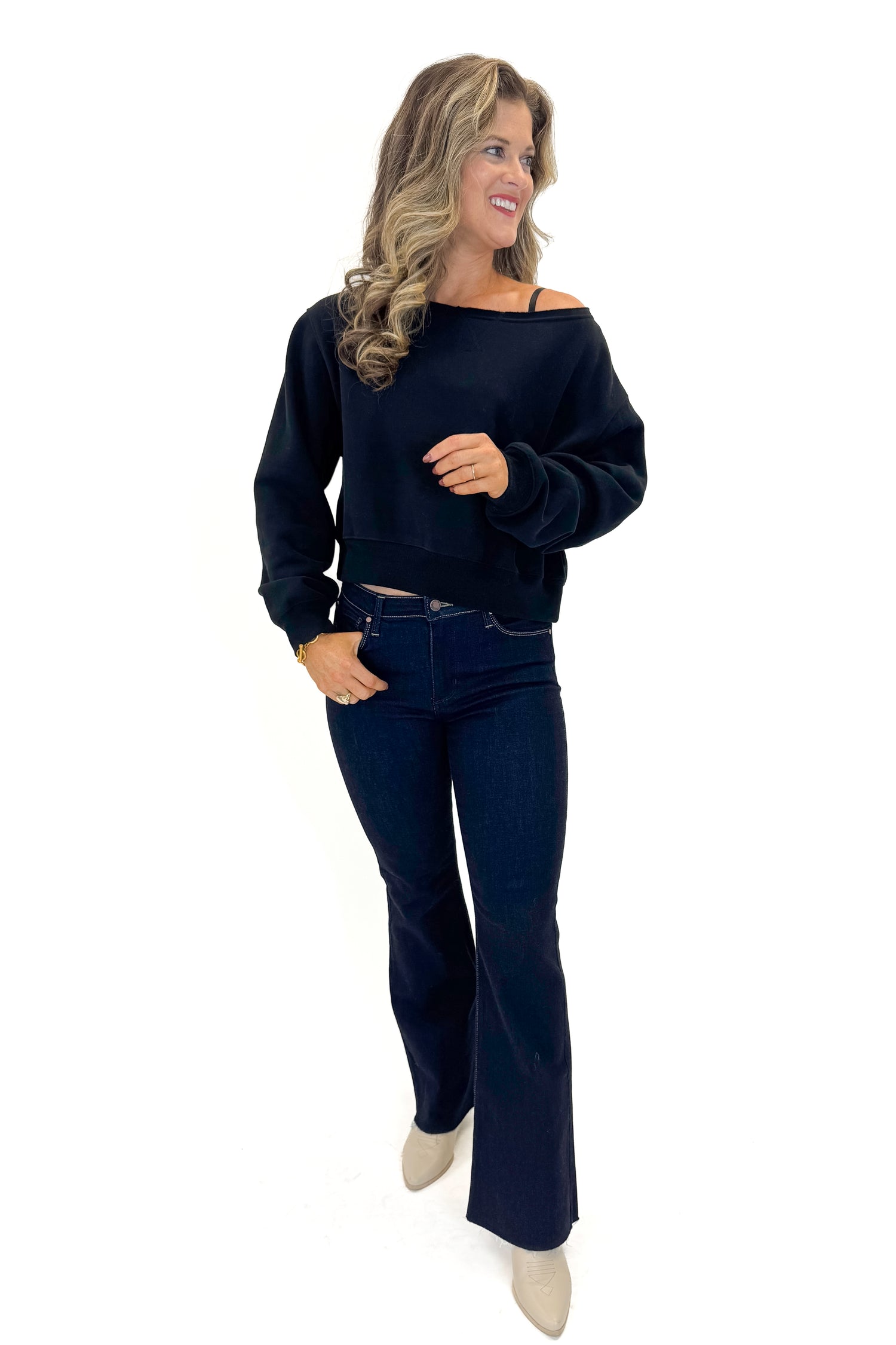 Front view of woman wearing Black Boatneck Banded Sweatshirt with jeans against white studio background.