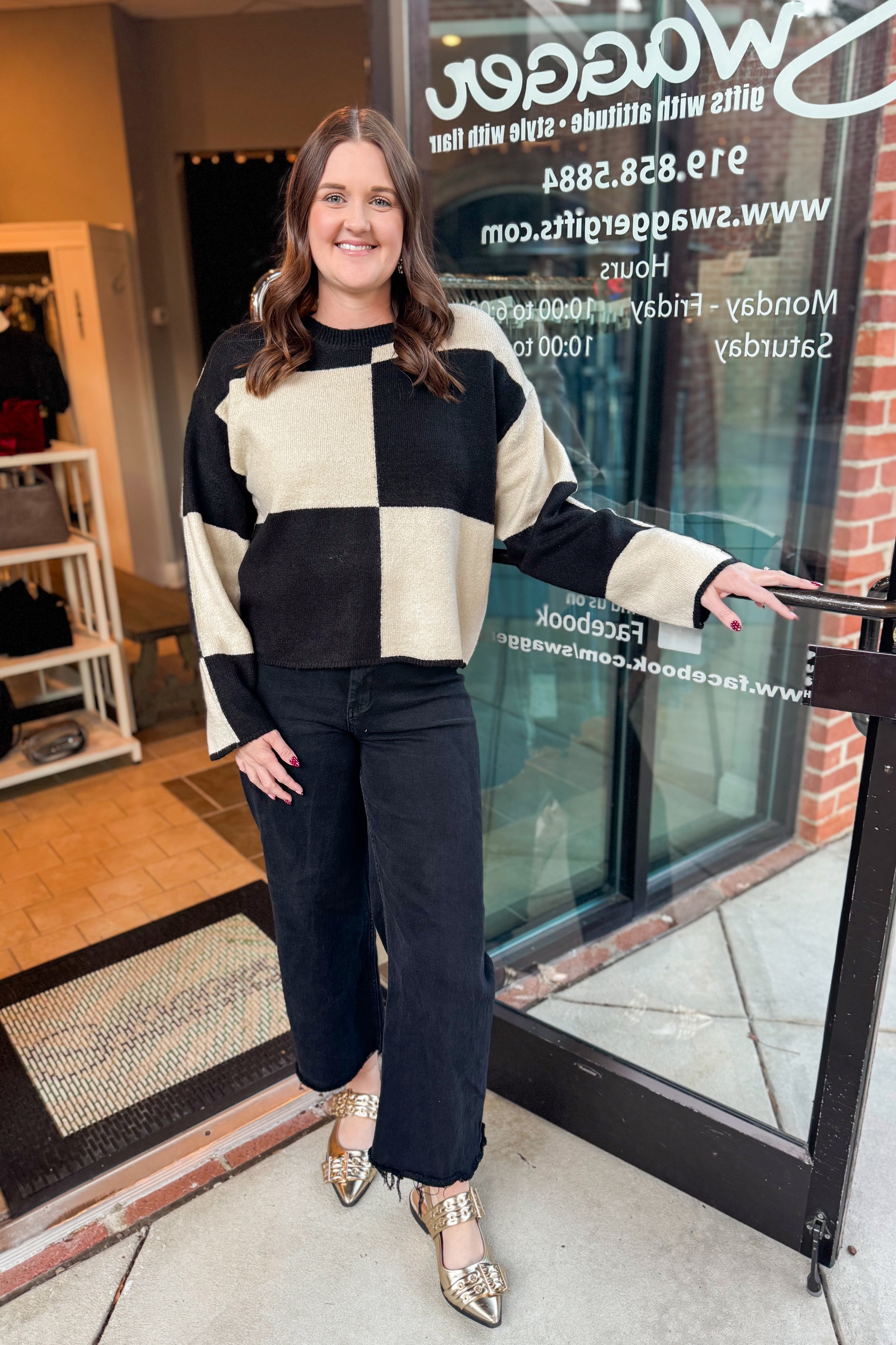 Front view of woman wearing Black &amp; Cream Checkered Sweater with jeans at a boutique.