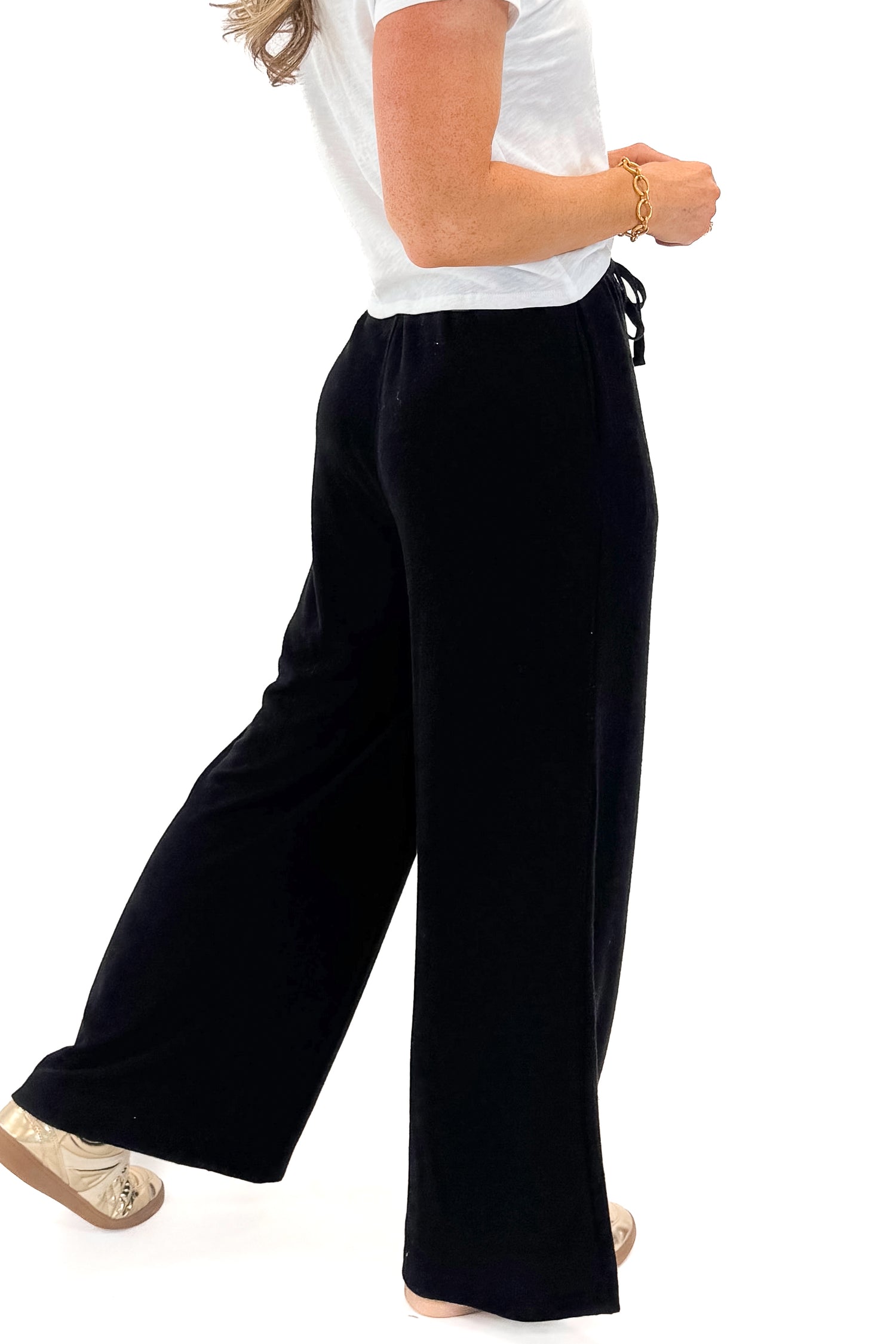 Side view of woman wearing Black Brushed Wide Leg Sweatpants with white top against white studio background.