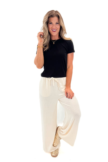 Front view of woman wearing black top with Cream Brushed Wide Leg Sweatpants against white studio background.