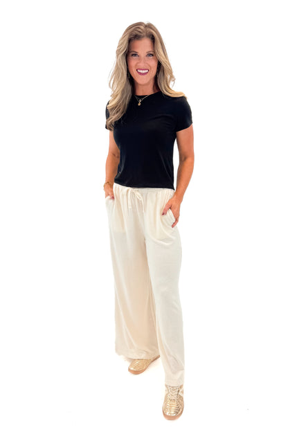 Front view of woman wearing black top with Cream Brushed Wide Leg Sweatpants against white studio background.