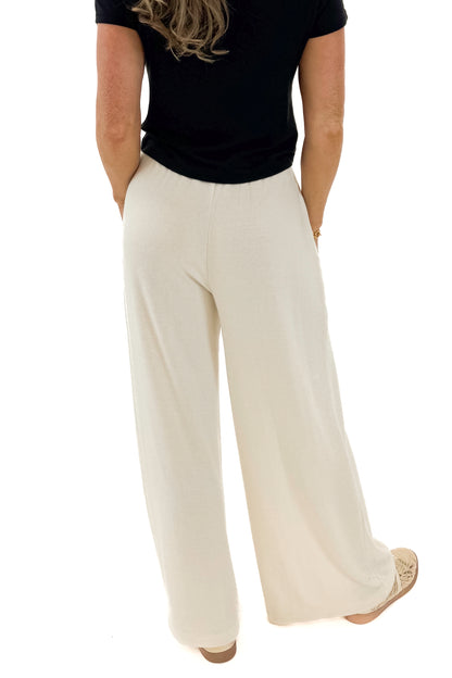 Back detail view of woman wearing black top with Cream Brushed Wide Leg Sweatpants against white studio background.
