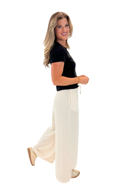 Side view of woman wearing black top with Cream Brushed Wide Leg Sweatpants against white studio background.