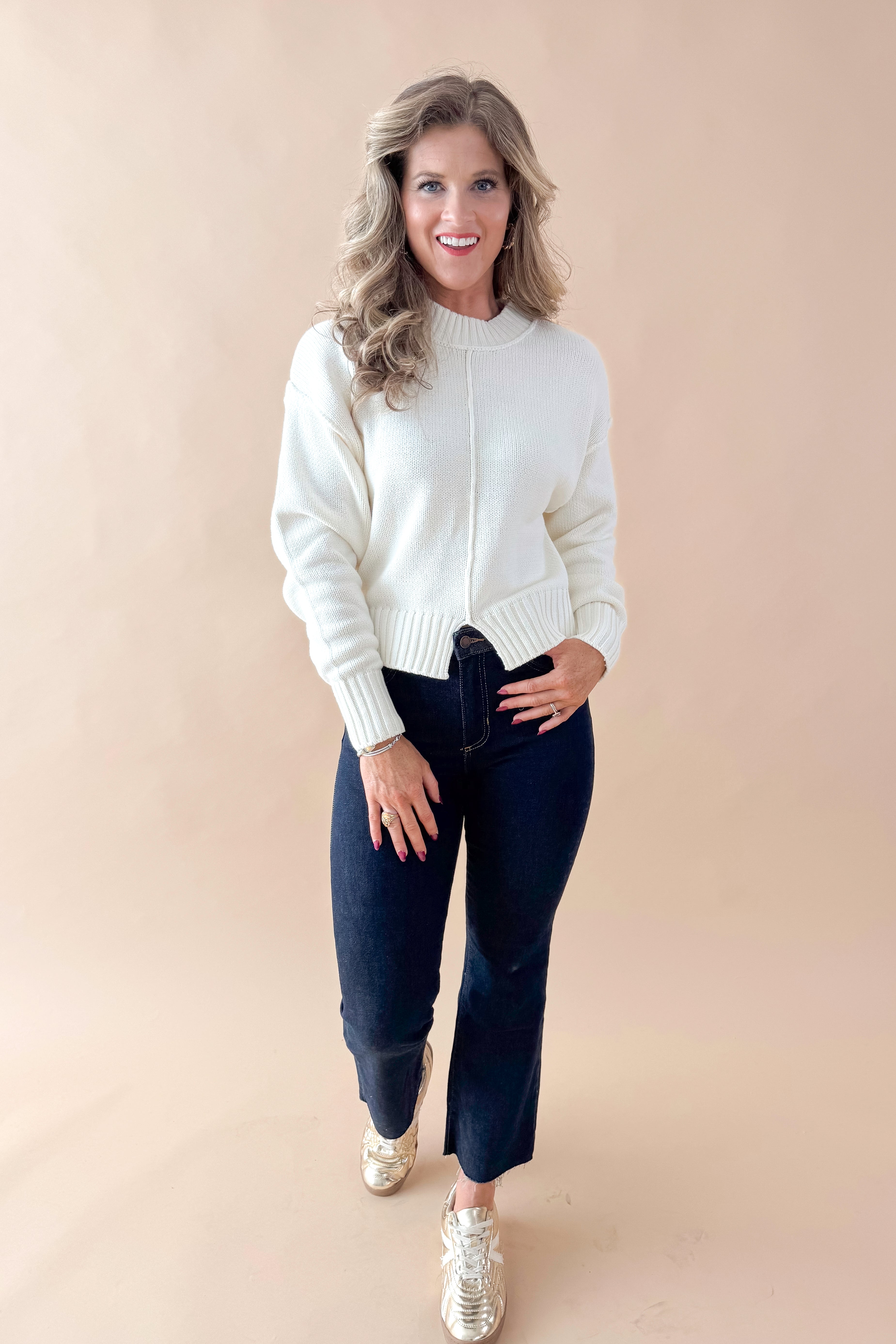 Front view of woman wearing Cream Seam Split Detail Sweater with jeans against tan studio background.