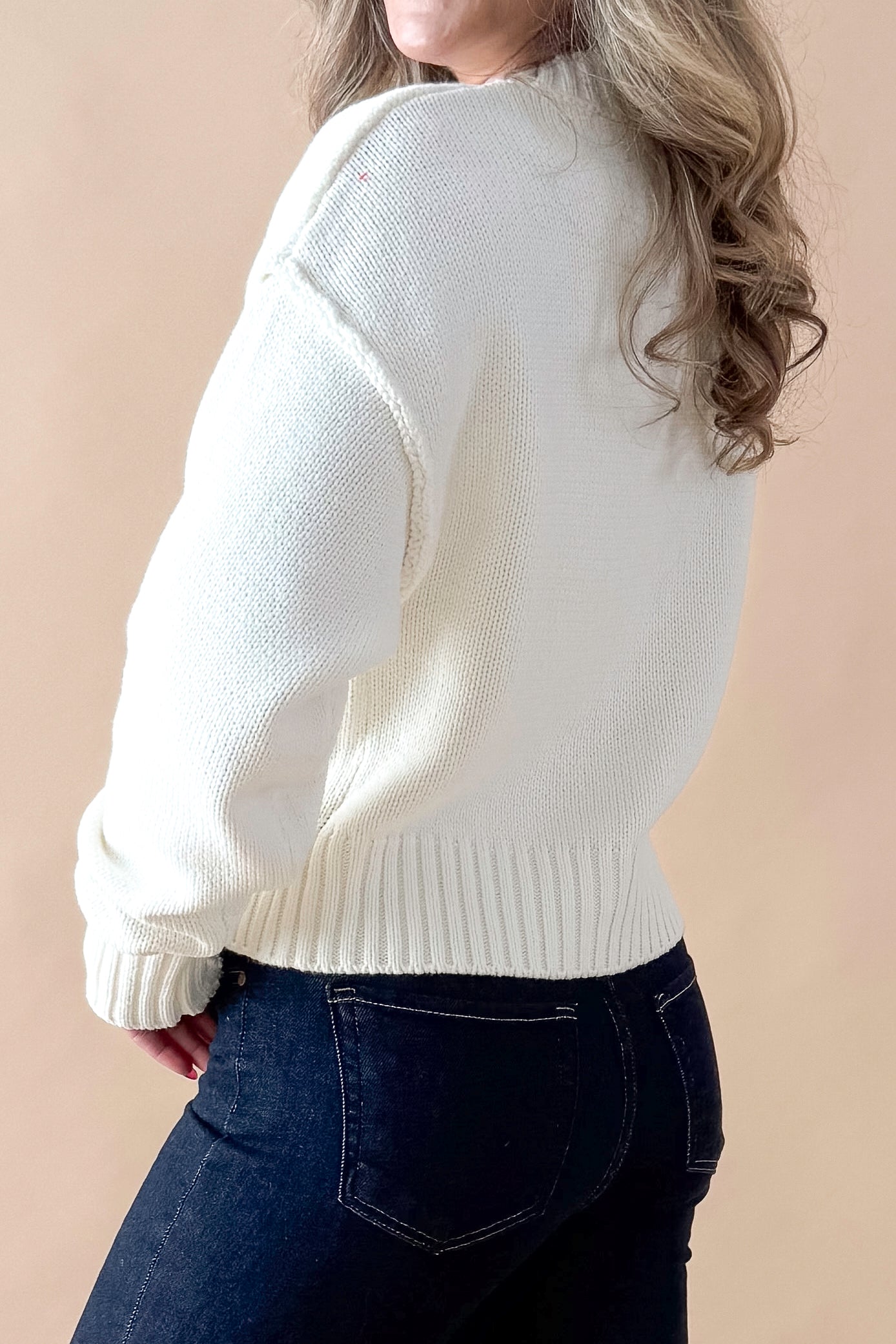 Side view of woman wearing Cream Seam Split Detail Sweater with jeans against tan studio background.