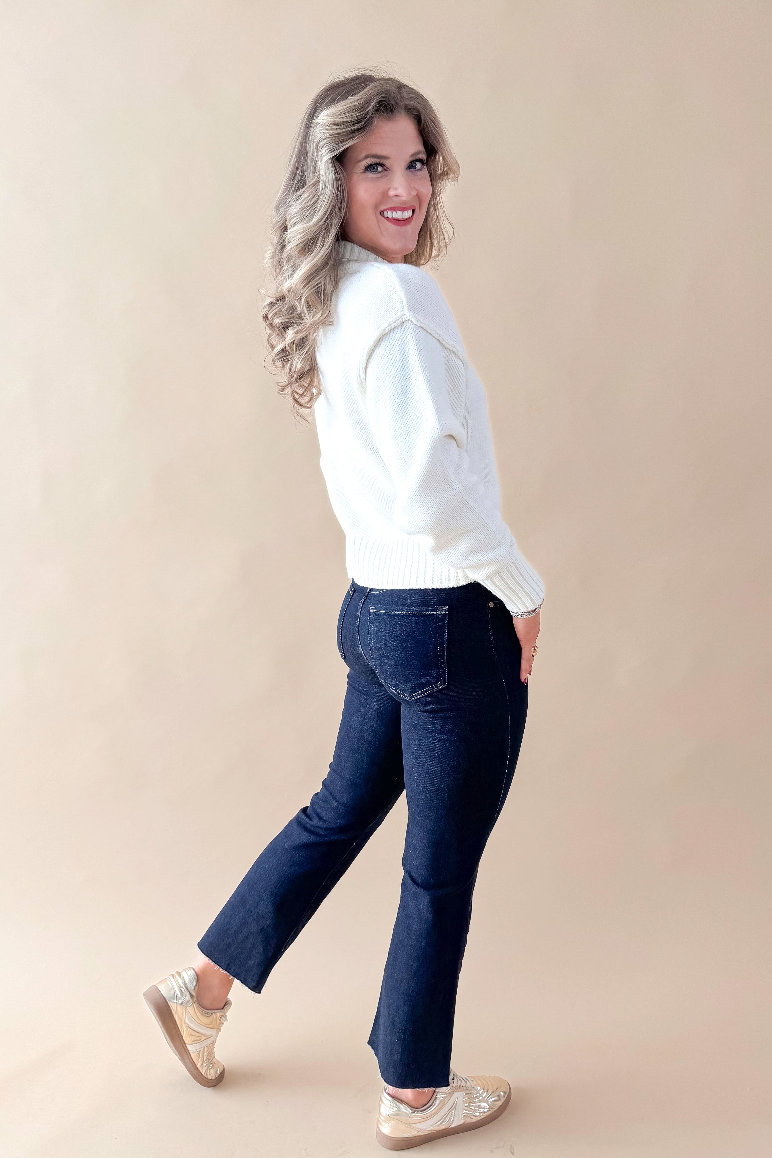 Side view of woman wearing Cream Seam Split Detail Sweater with jeans against tan studio background.