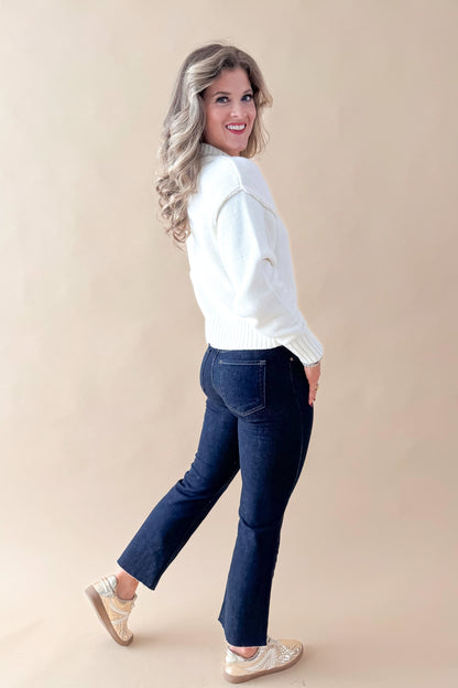 Side view of woman wearing Cream Seam Split Detail Sweater with jeans against tan studio background.
