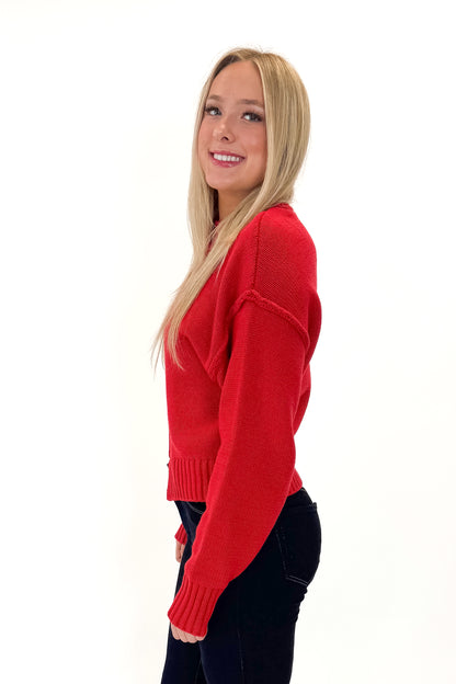 Side view of woman wearing Red Seam Split Detail Sweater with jeans against white studio background.