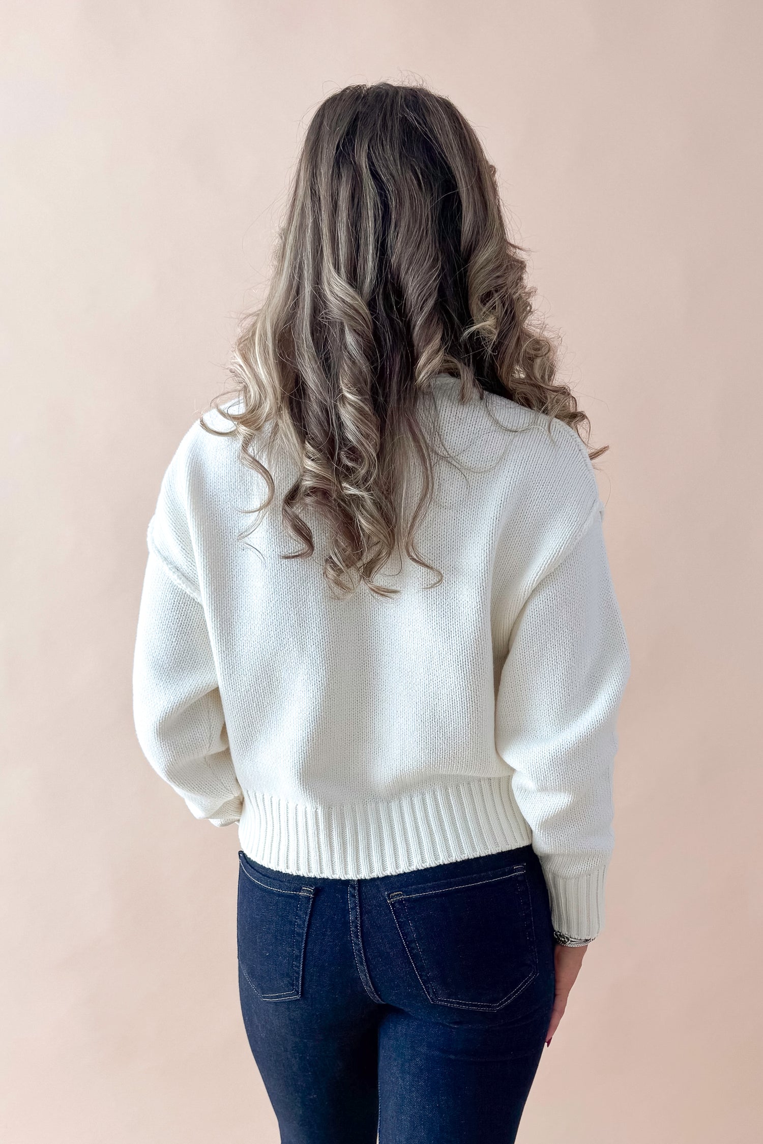 Back view of woman wearing Cream Seam Split Detail Sweater with jeans against tan studio background.