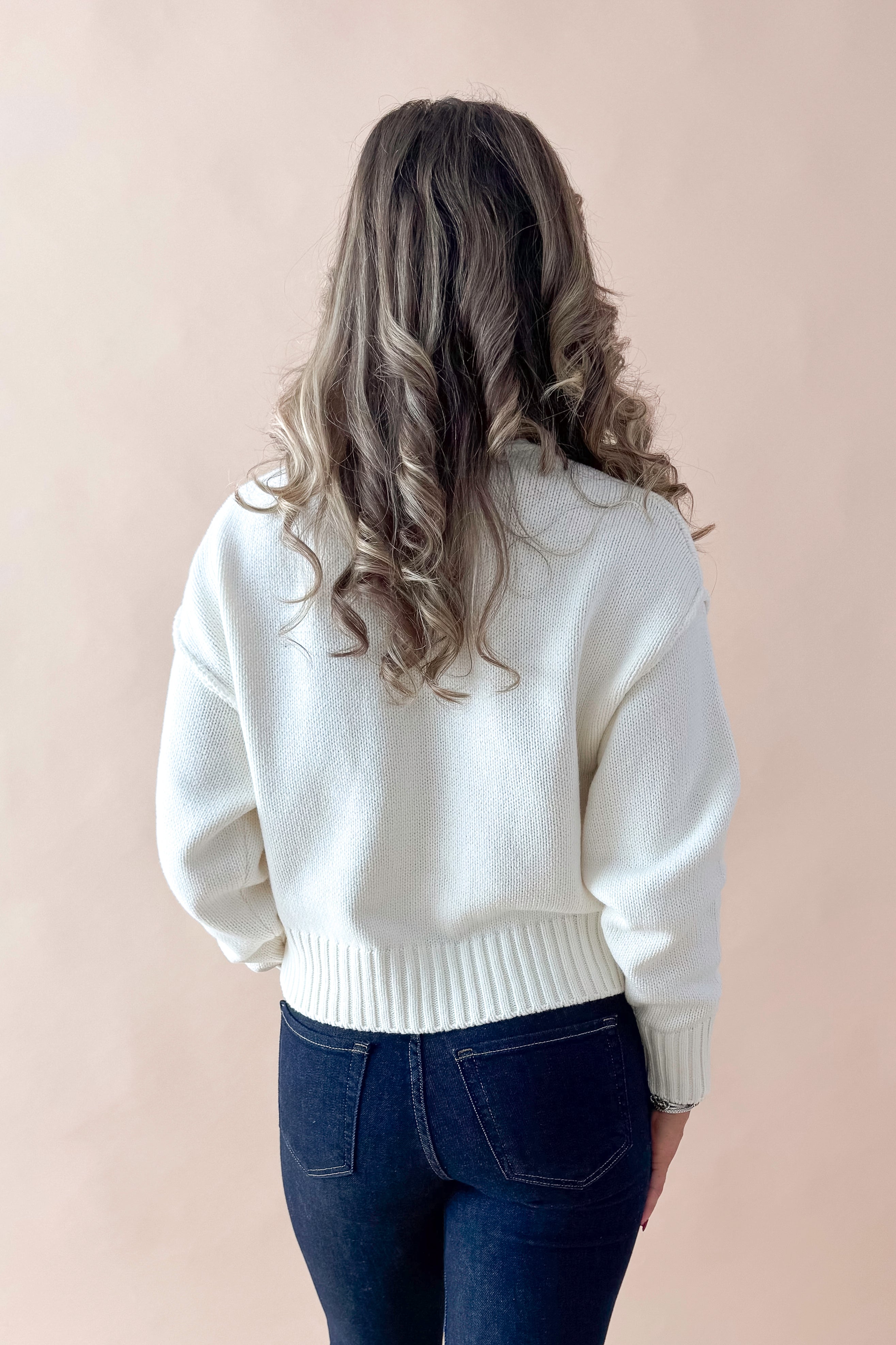 Back view of woman wearing Cream Seam Split Detail Sweater with jeans against tan studio background.