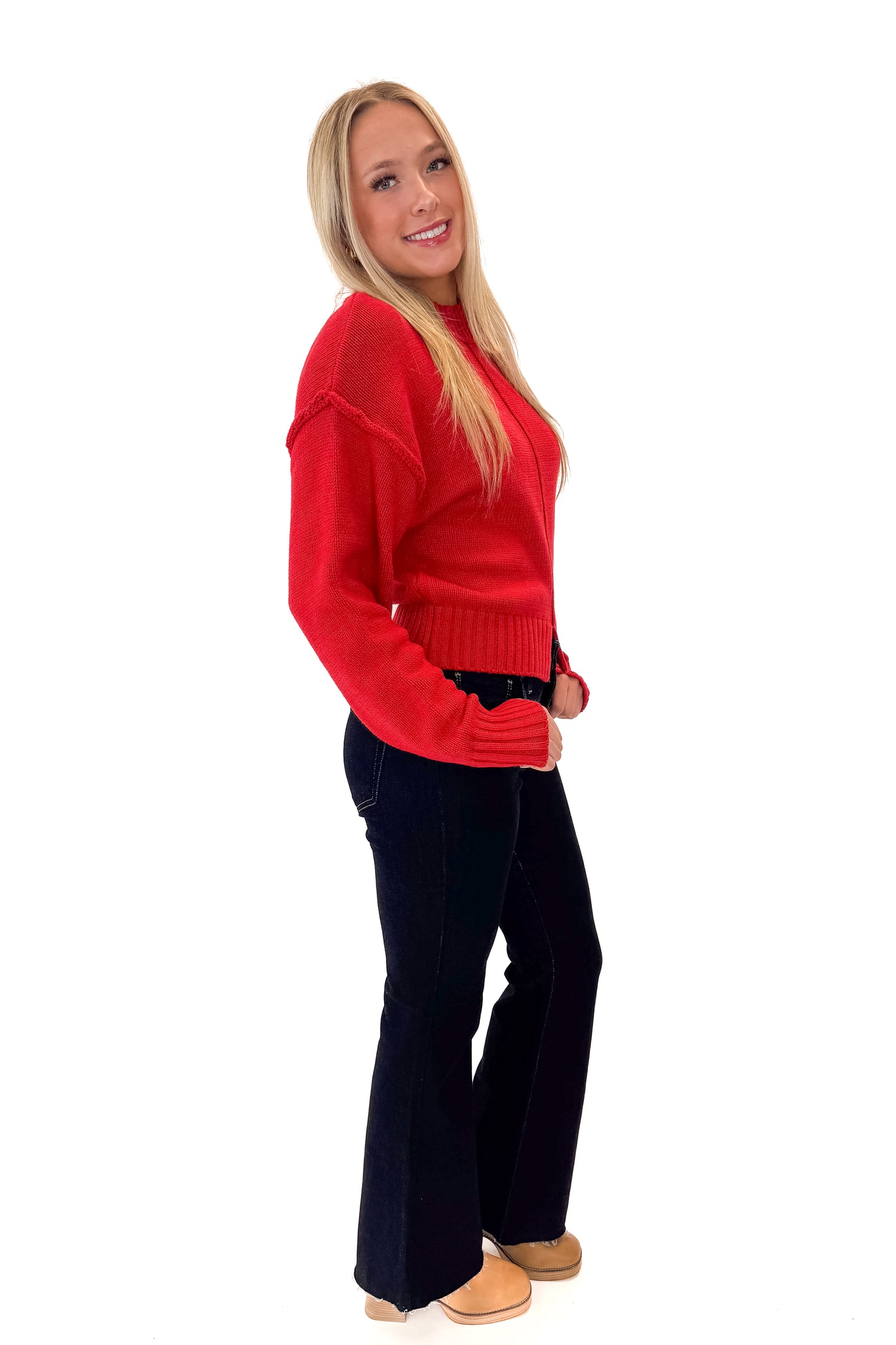 Side view of woman wearing Red Seam Split Detail Sweater with jeans against white studio background.