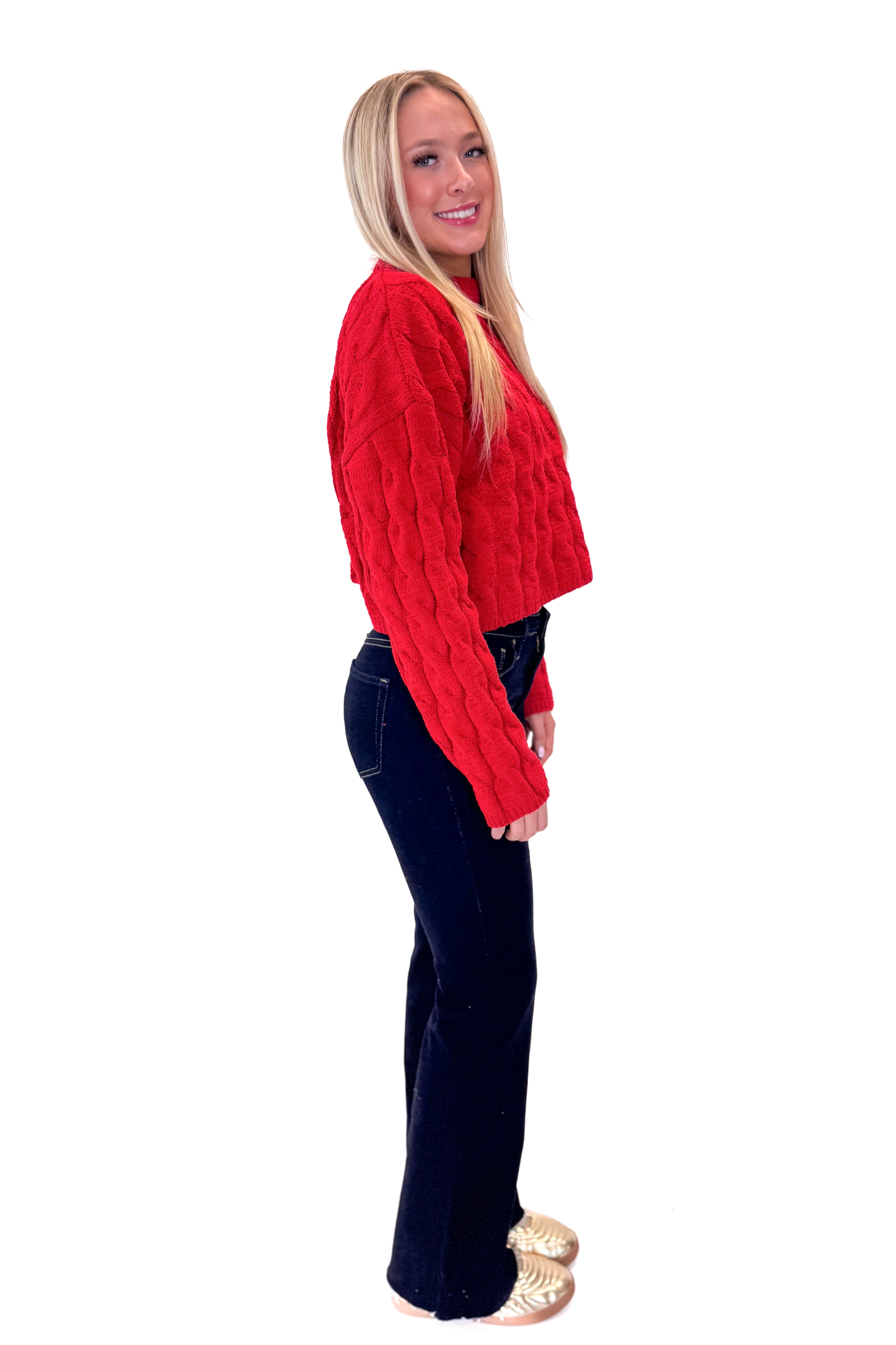 Side view of woman wearing Red Textured Cable Knit Sweater with skirt against white studio background.