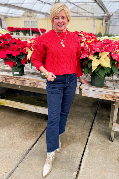 Front view of woman wearing Red Textured Cable Knit Sweater with jeans by holiday decor.