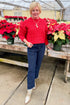 Front view of woman wearing Red Textured Cable Knit Sweater with jeans by holiday decor.