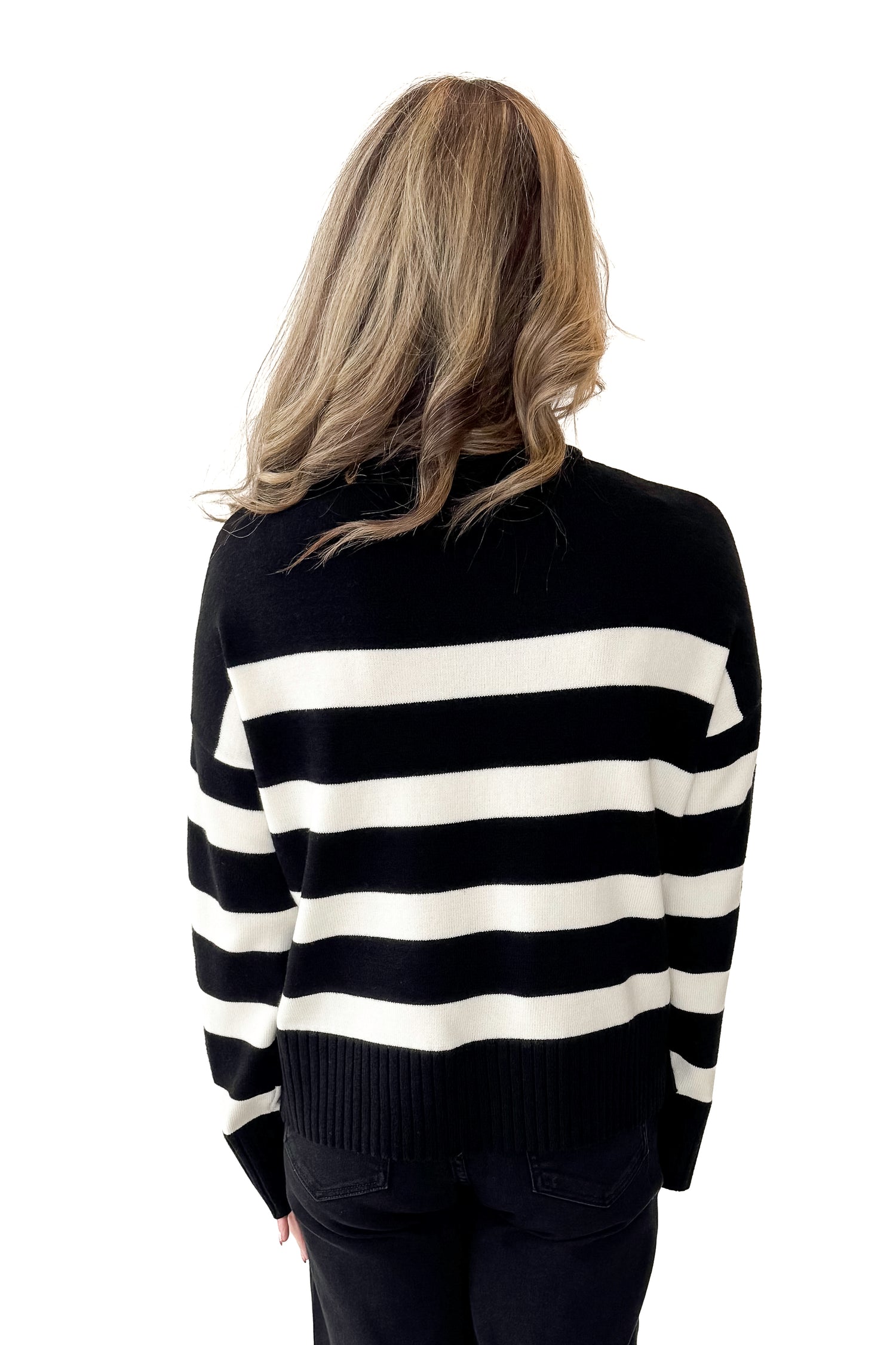 Back view of woman wearing Black and Cream Striped Crewneck Sweater with jeans against white studio background.