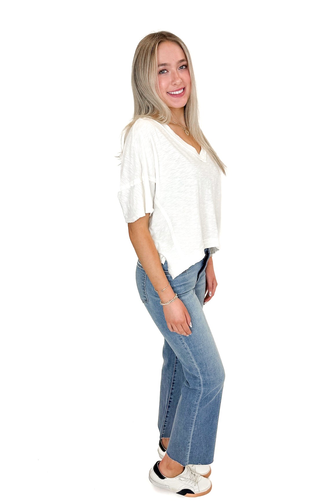 Side view of woman wearing Cream V-Neck Tee with jeans against white studio background