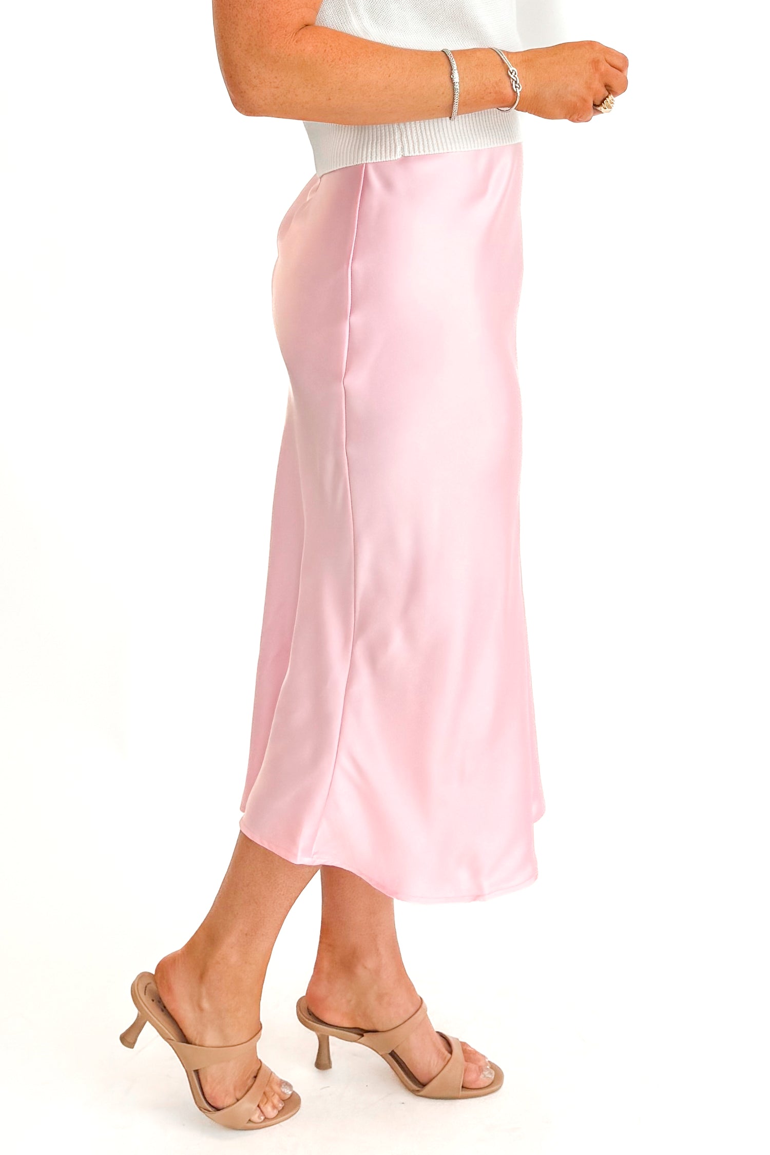 Side view of woman wearing Soft Pink Satin Skirt with white cap sleeve sweater against white studio background.