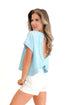 Side view of woman wearing Light Blue Cut Out Back Tee with jean shorts against white studio background.