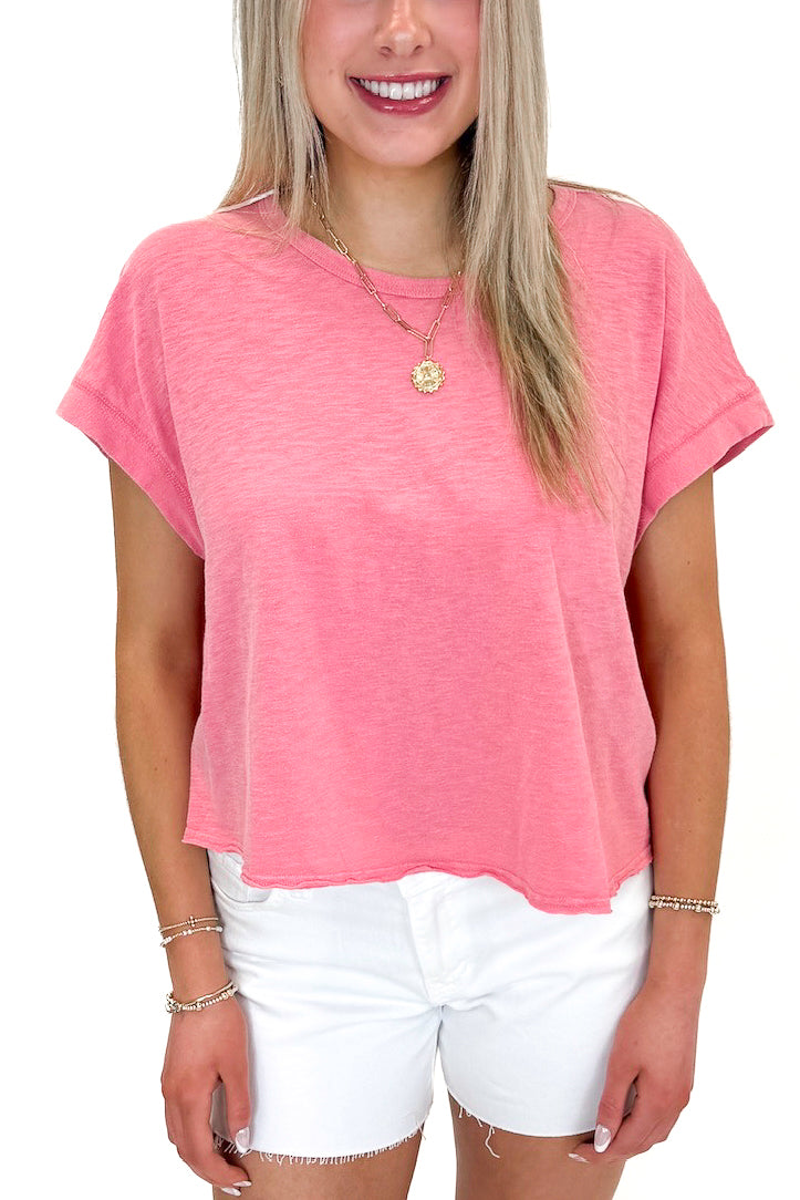 Front view of woman wearing Pink Cut Out Back Tee with jean shorts against white studio background.