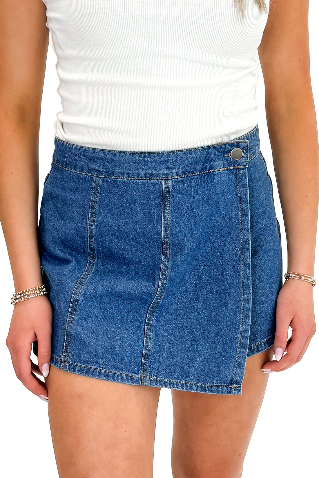 Front detail view of woman wearing white top with Medium Wash Denim Wrap Skort against white studio background.