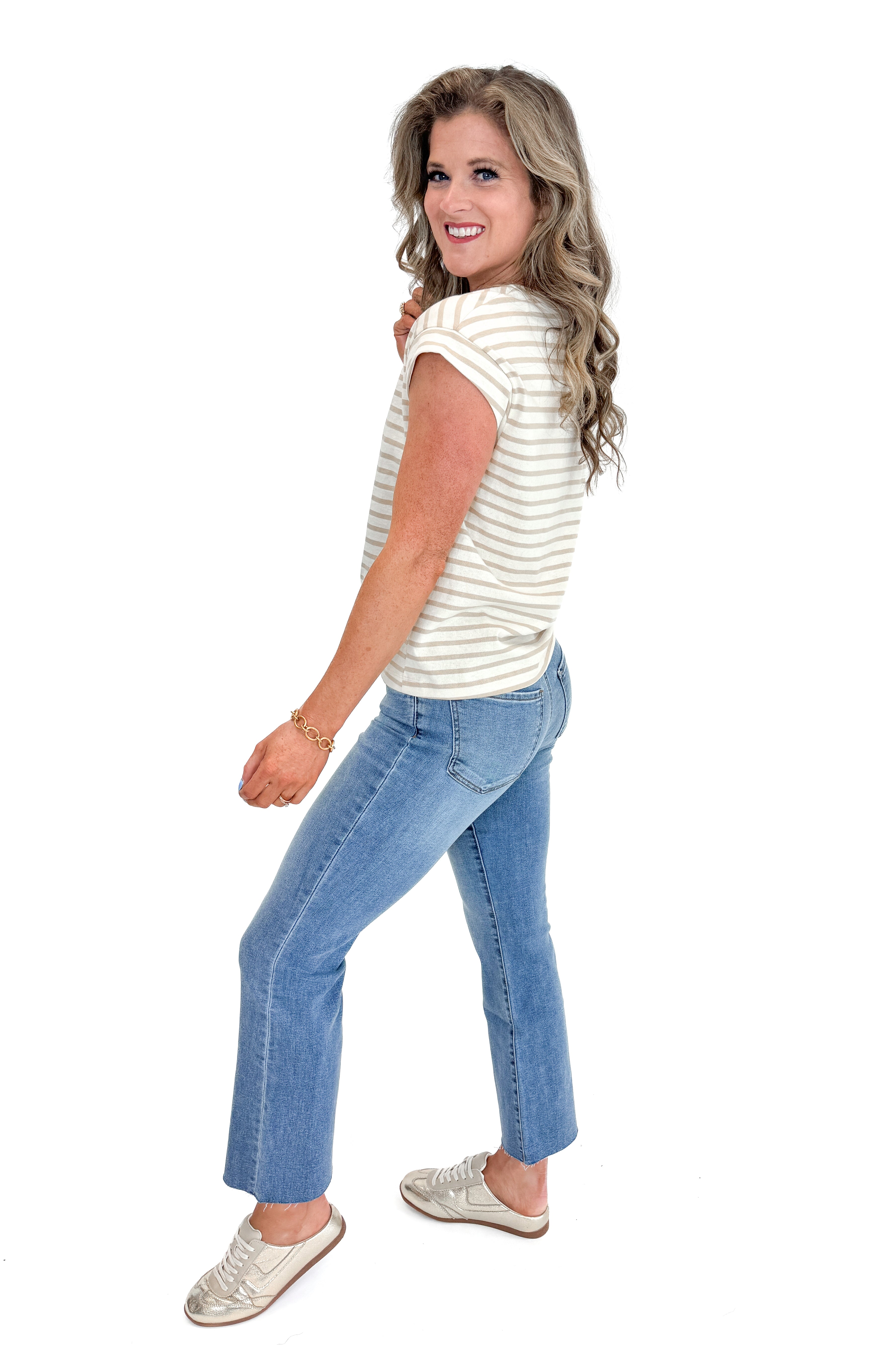 Side view of woman wearing Taupe &amp; Cream Stripe Cap Sleeve Tee with jeans against white studio background.
