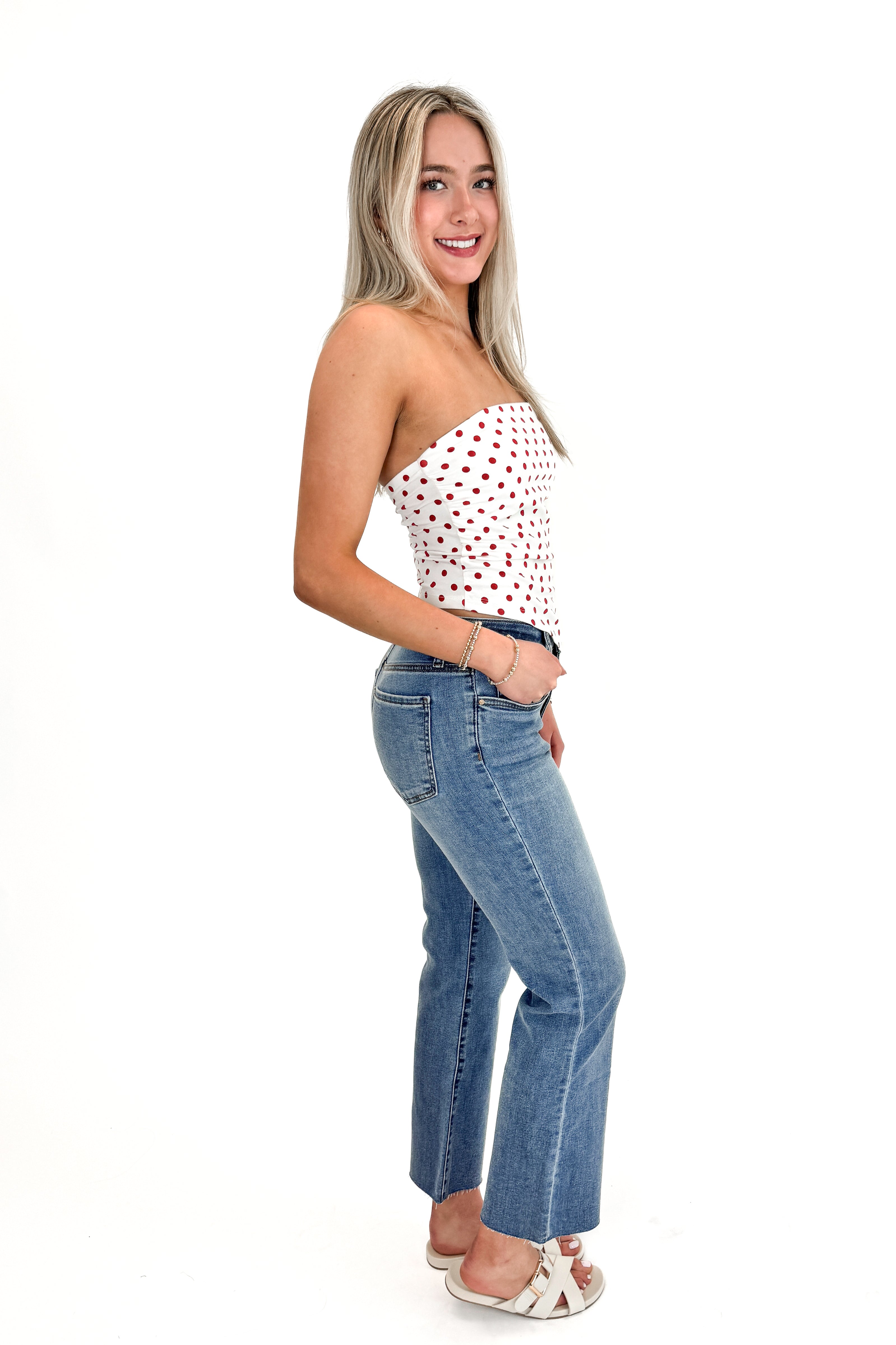 Side view of woman wearing Red Polka Dot Strapless Top with jeans against white studio background.