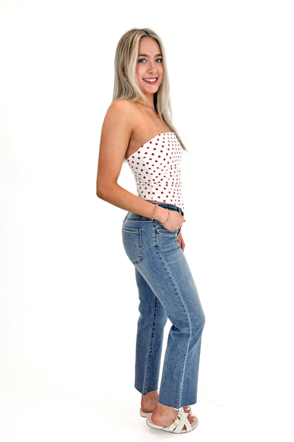 Side view of woman wearing Red Polka Dot Strapless Top with jeans against white studio background.
