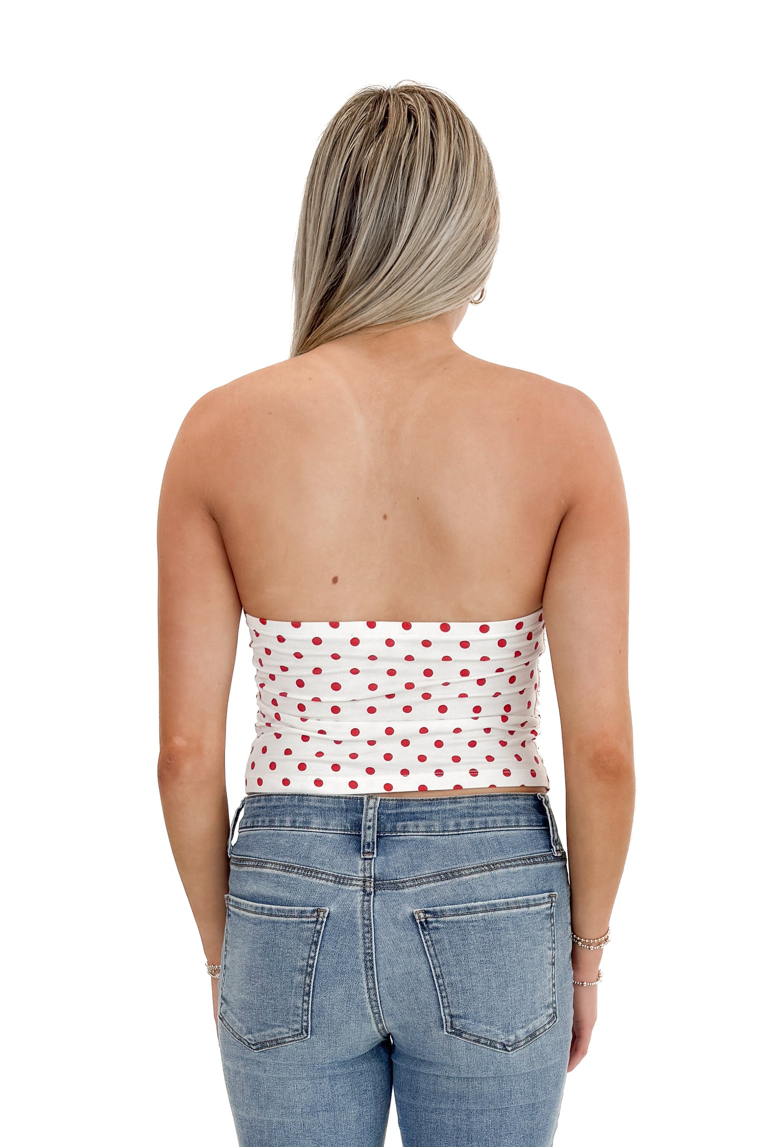 Back view of woman wearing Red Polka Dot Strapless Top with jeans against white studio background.