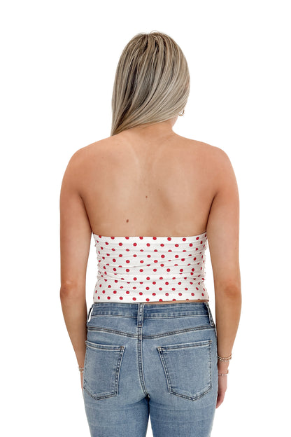 Back view of woman wearing Red Polka Dot Strapless Top with jeans against white studio background.