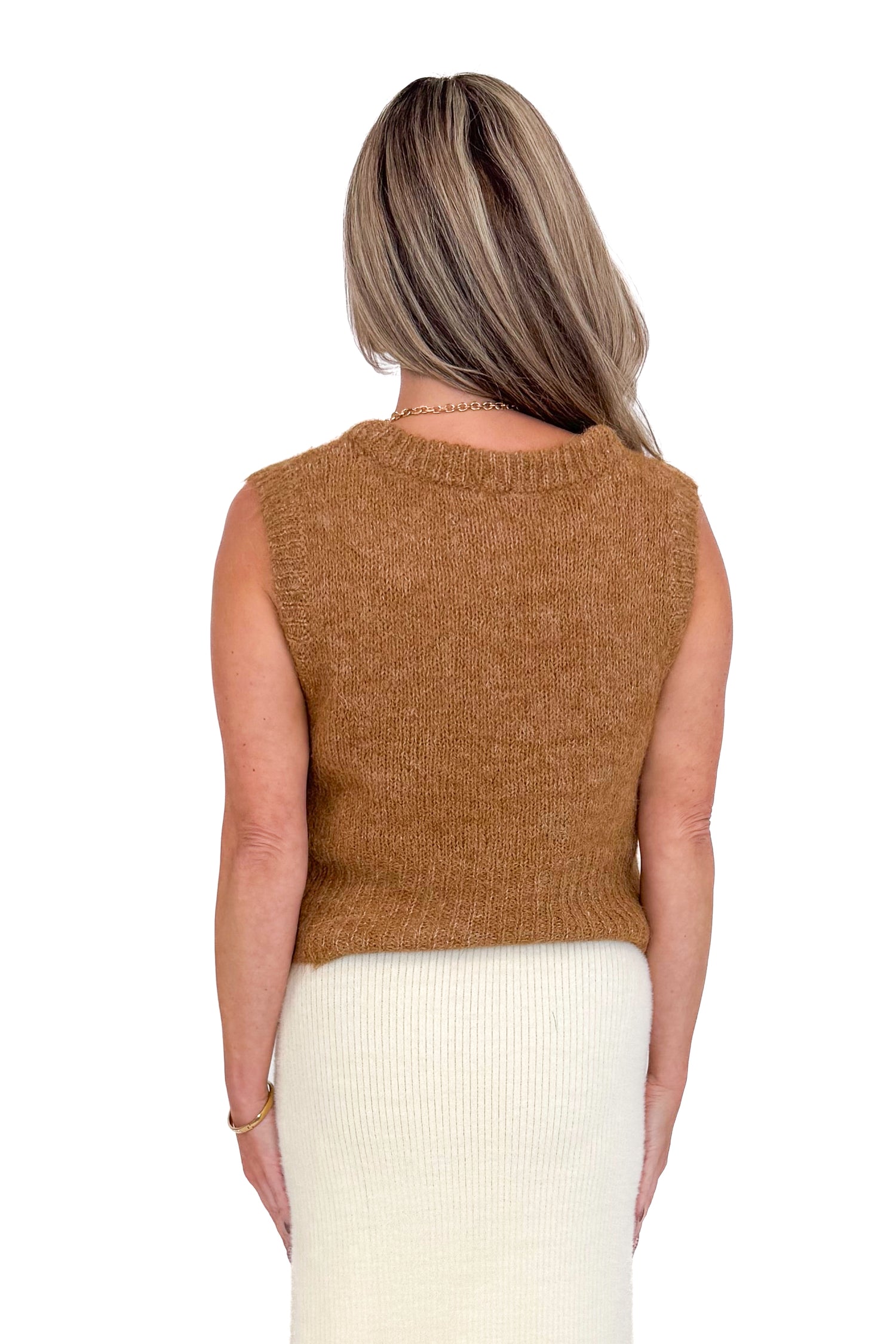 Back view of woman wearing caramel color sweater with cream skirt against white studio background.