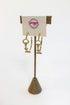 A pair of gold horse-bit style hoop earrings displayed on a textured stand with a branded card that reads &