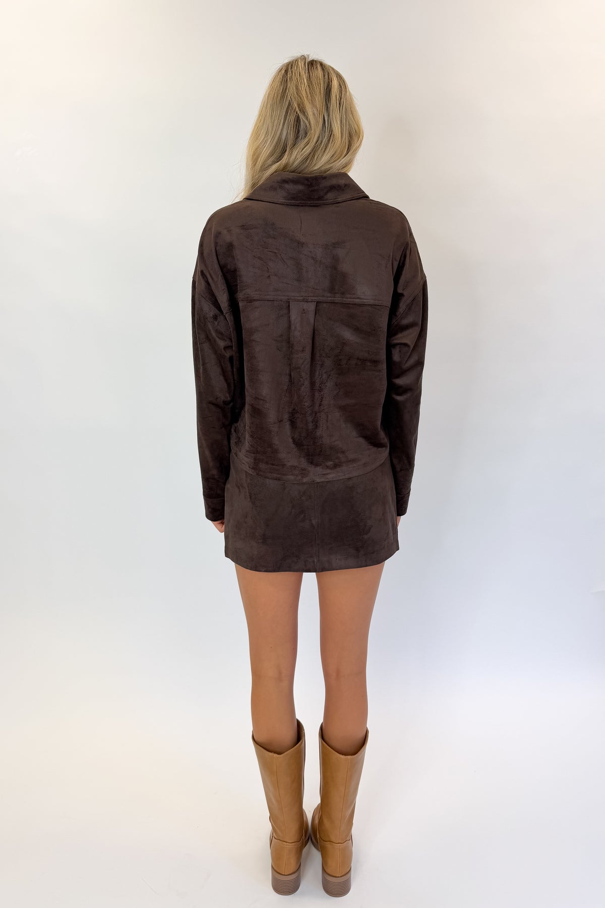 Back view of woman wearing Swagger Boutique’s All Day Cropped Suede Jacket and Perri Suede Mini Skirt by Z Supply In Dark Chocolate against white studio background.
